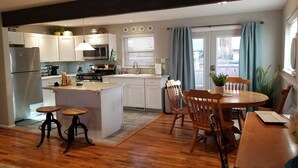 A modern kitchen with white cabinets, a central island, and wooden stools. - Hillside Cottage In The Pines With Great Views (Williams)