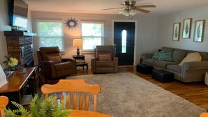A living room with a fireplace, two armchairs, a sofa, a dining table with chairs, and a ceiling fan. - Hillside Cottage In The Pines With Great Views (Williams)