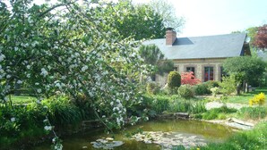 A serene garden with a pond, lush greenery, and a stone building with a sloped roof.