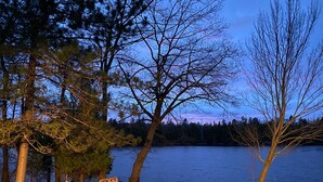 A lakeside setting with a fire pit, benches, and trees. - Your Northwoods Waterfront Getaway (Crivitz)