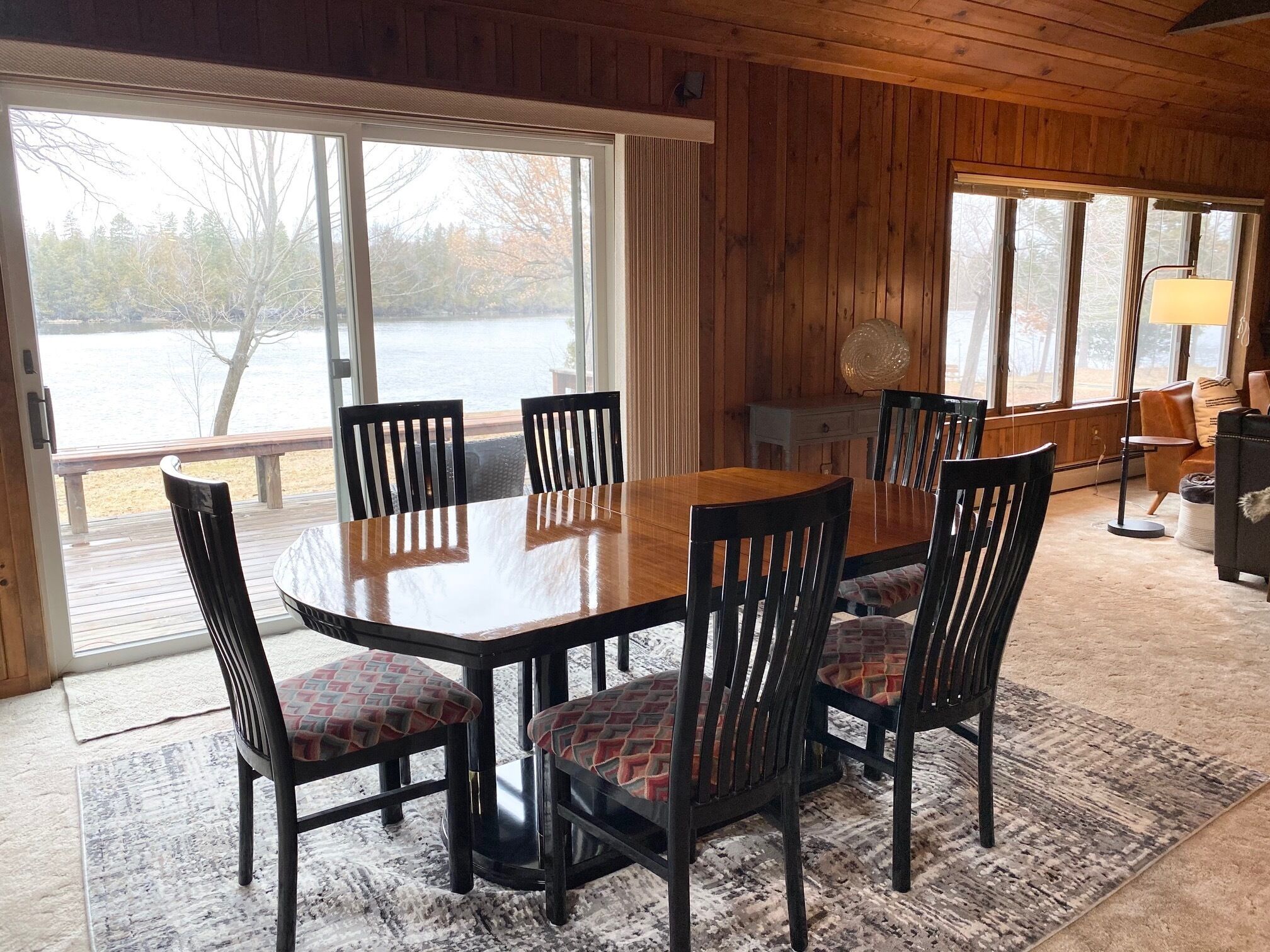 Un intérieur en bois avec une table et des chaises, de grandes fenêtres et une vue sur une étendue d’eau.