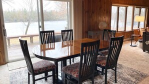 A wooden interior with a dining table and chairs, large windows, and a view of a body of water. - Your Northwoods Waterfront Getaway (Crivitz)