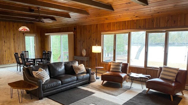 A cozy living room with a leather sofa, armchairs, and a coffee table. Large windows offer a view of the outdoors. - Your Northwoods Waterfront Getaway (Crivitz)