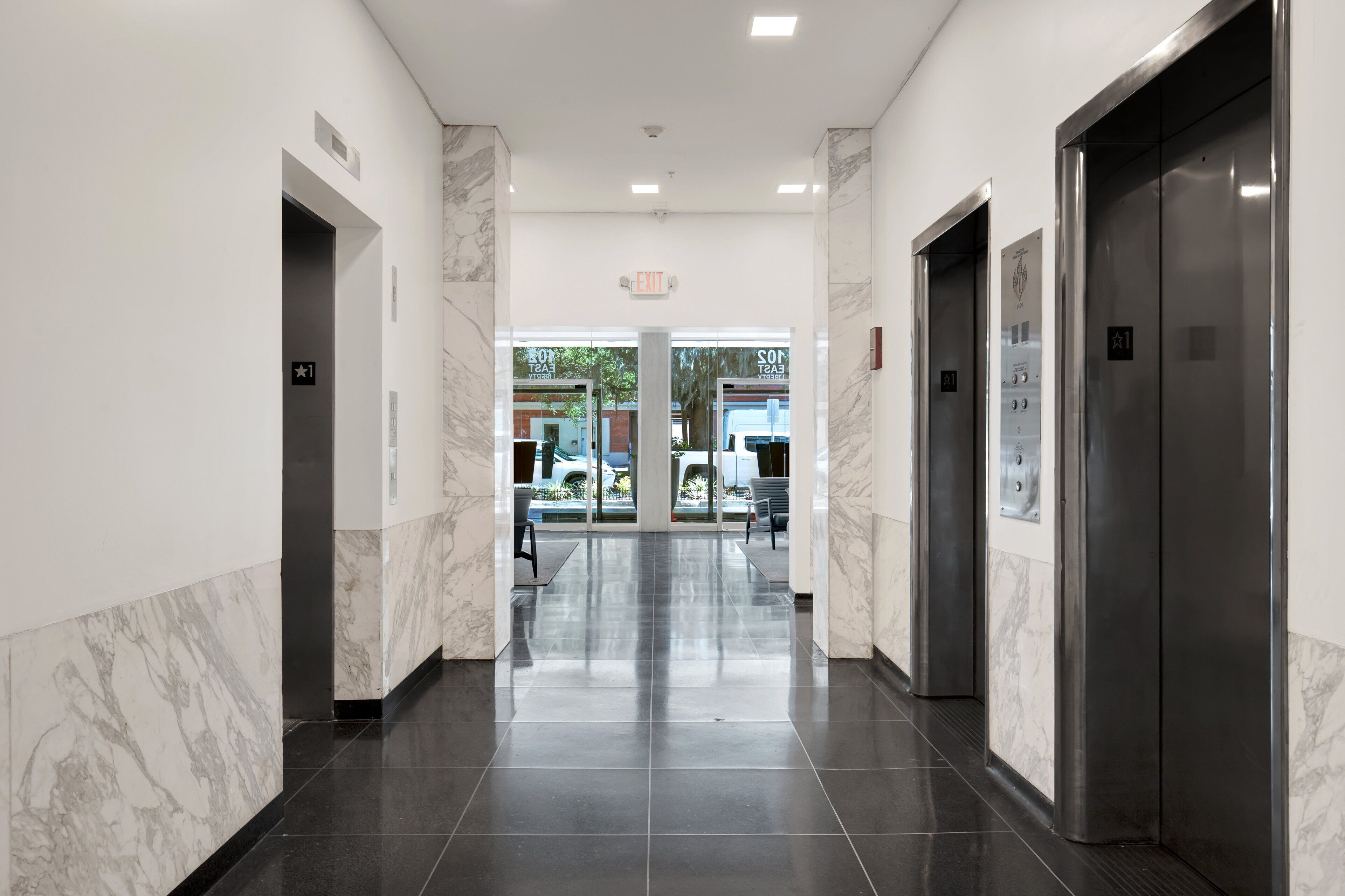 A modern hotel corridor with marble walls, black tiled floors, and two elevators.