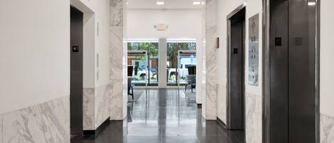 A modern hotel corridor with marble walls, black tiled floors, and two elevators.