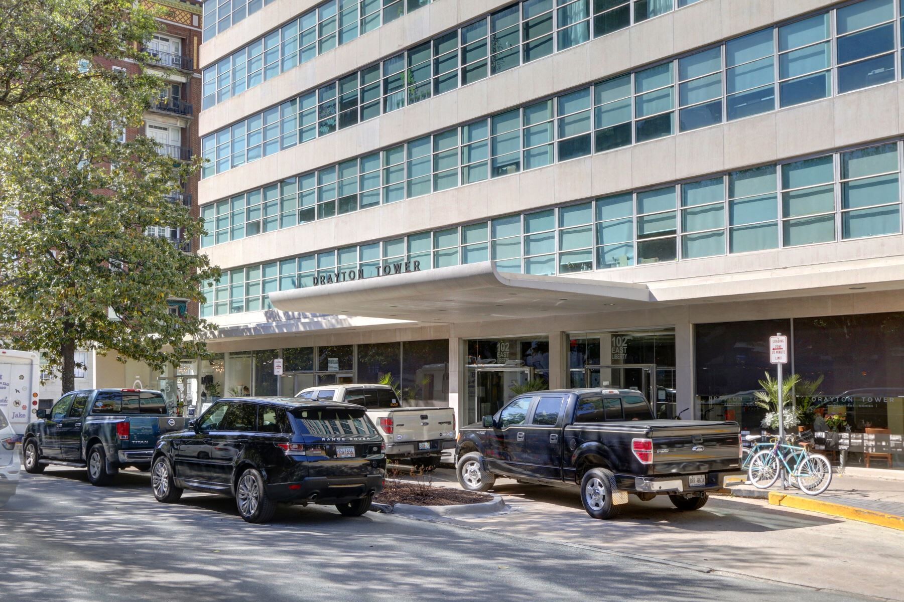 A multi-story building with a modern facade, a covered entrance, and several parked vehicles including SUVs and a pickup truck.