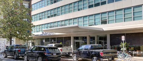 A multi-story building with a modern facade, a covered entrance, and several parked vehicles including SUVs and a pickup truck.