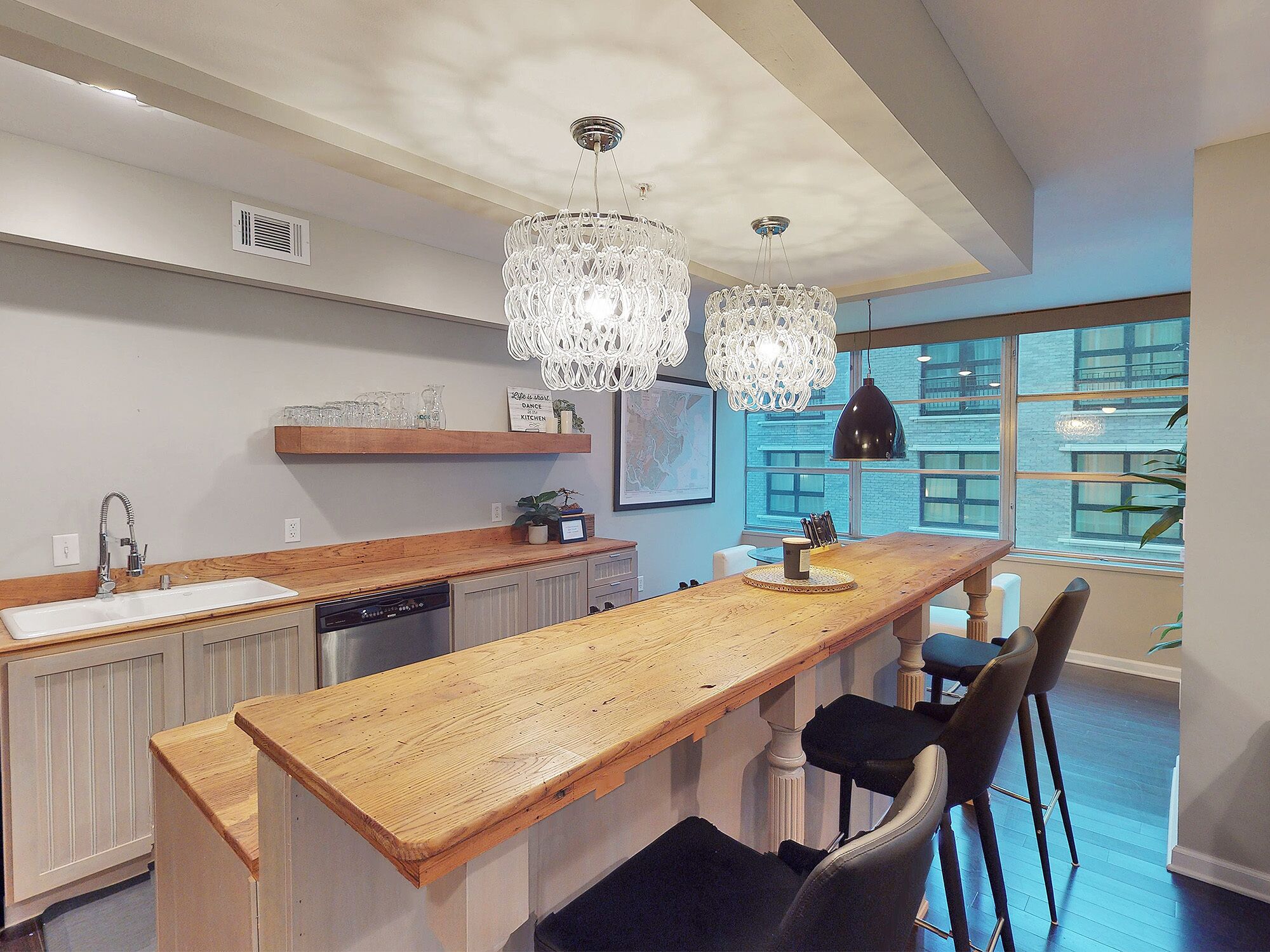 Une cuisine moderne avec un îlot central en bois, des luminaires suspendus et une vue sur la ville grâce à de grandes fenêtres.