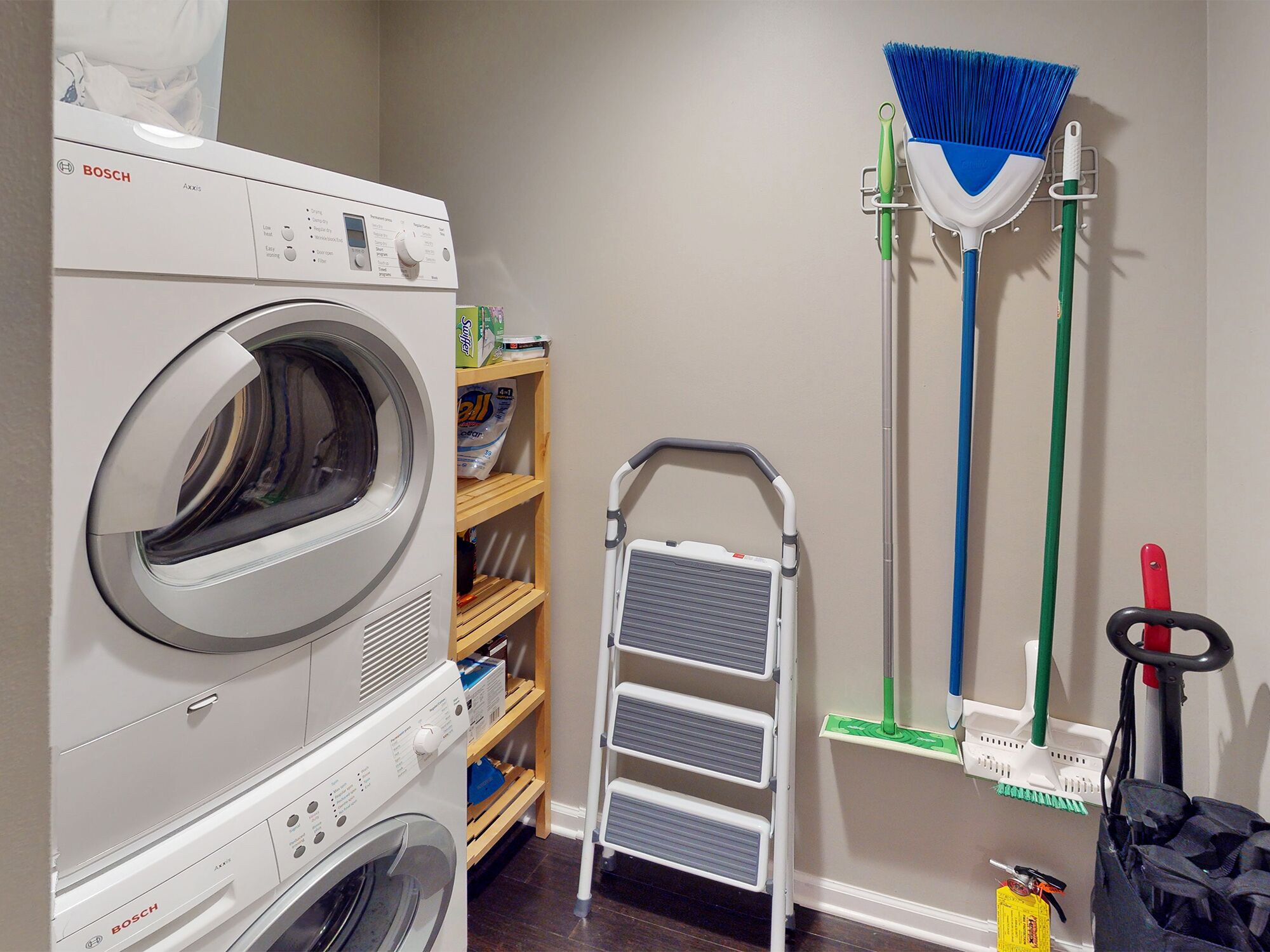 A laundry area with a Bosch washing machine, a mop, a broom, and a mop bucket.