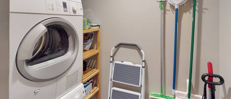 A laundry area with a Bosch washing machine, a mop, a broom, and a mop bucket.