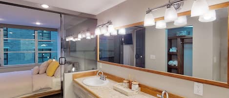 A modern bathroom with two sinks, a large mirror, and a bed with a view of the city.
