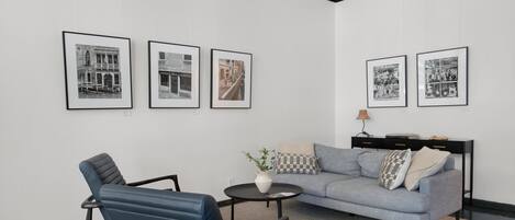 A modern room with a grey sofa, a blue chair, a small round table with a vase, and four framed pictures on the wall.