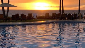 Une piscine avec vue sur le coucher de soleil, des chaises longues et des palmiers.