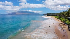 Une plage aux eaux turquoise et limpides, un rivage sablonneux et une montagne en arrière-plan.