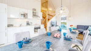 A modern kitchen with white cabinets, a microwave, and a stove. There is a dining area with a table set for two, blue cups, and a vase with flowers. - Pet friendly home in OstseeResort Olpenitz with sauna (OstseeResort Olpenitz)