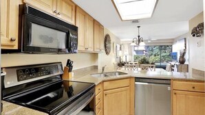 Une cuisine moderne avec des meubles en bois, un micro-ondes noir, des appareils électroménagers en acier inoxydable et un puits de lumière.