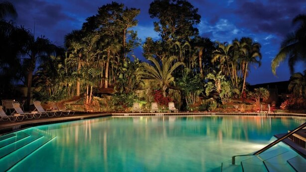 Un espace piscine aménagé pour la nuit, avec des chaises longues et une végétation tropicale.