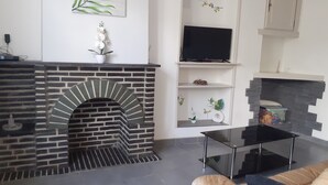 A living room with a brick fireplace, a flat-screen TV, a glass coffee table, and a sofa. - The house of happiness ⭐⭐⭐ (Fumay)