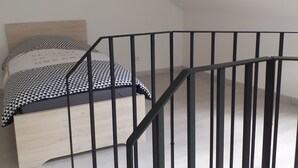 A bedroom with a bed, a black metal railing, and a ceiling with exposed beams. - The house of happiness ⭐⭐⭐ (Fumay)