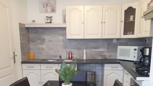 A modern kitchen with white cabinets, a black countertop, a microwave, a coffee maker, and a dining table with chairs. - The house of happiness ⭐⭐⭐ (Fumay)