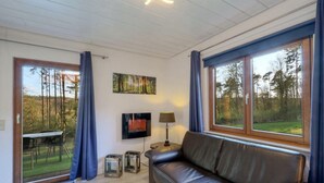 Ein modernes Wohnzimmer mit Ledersofa, Flachbildfernseher und einem Waldgemälde.