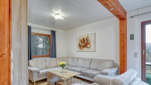 Ein modernes Wohnzimmer mit einem Ecksofa, einem Couchtisch und einem großen Fenster mit Vorhängen.