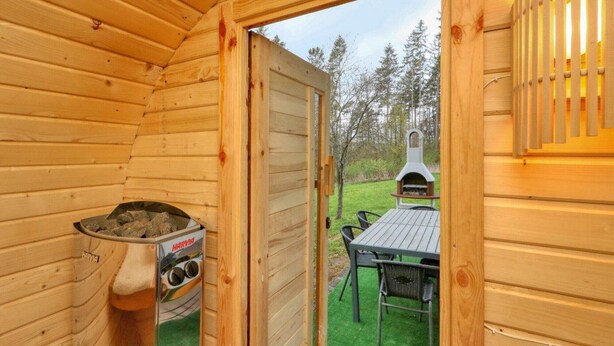 Eine Holzhütte mit einem Harvia Holzofen, einem Grill draußen und einem Tisch mit Stühlen.