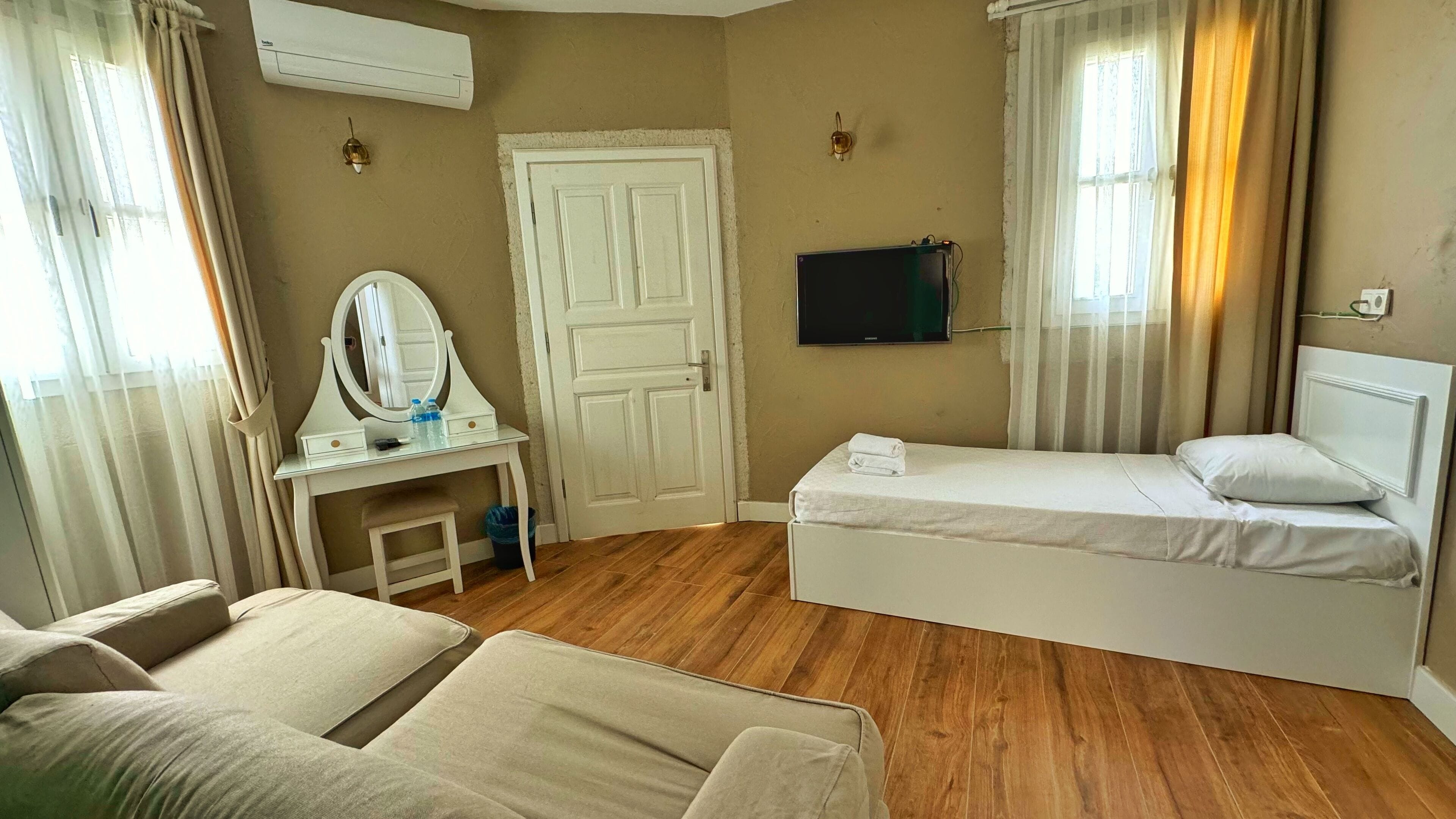 Una habitación de hotel con cama, escritorio con espejo, televisión y sofá.