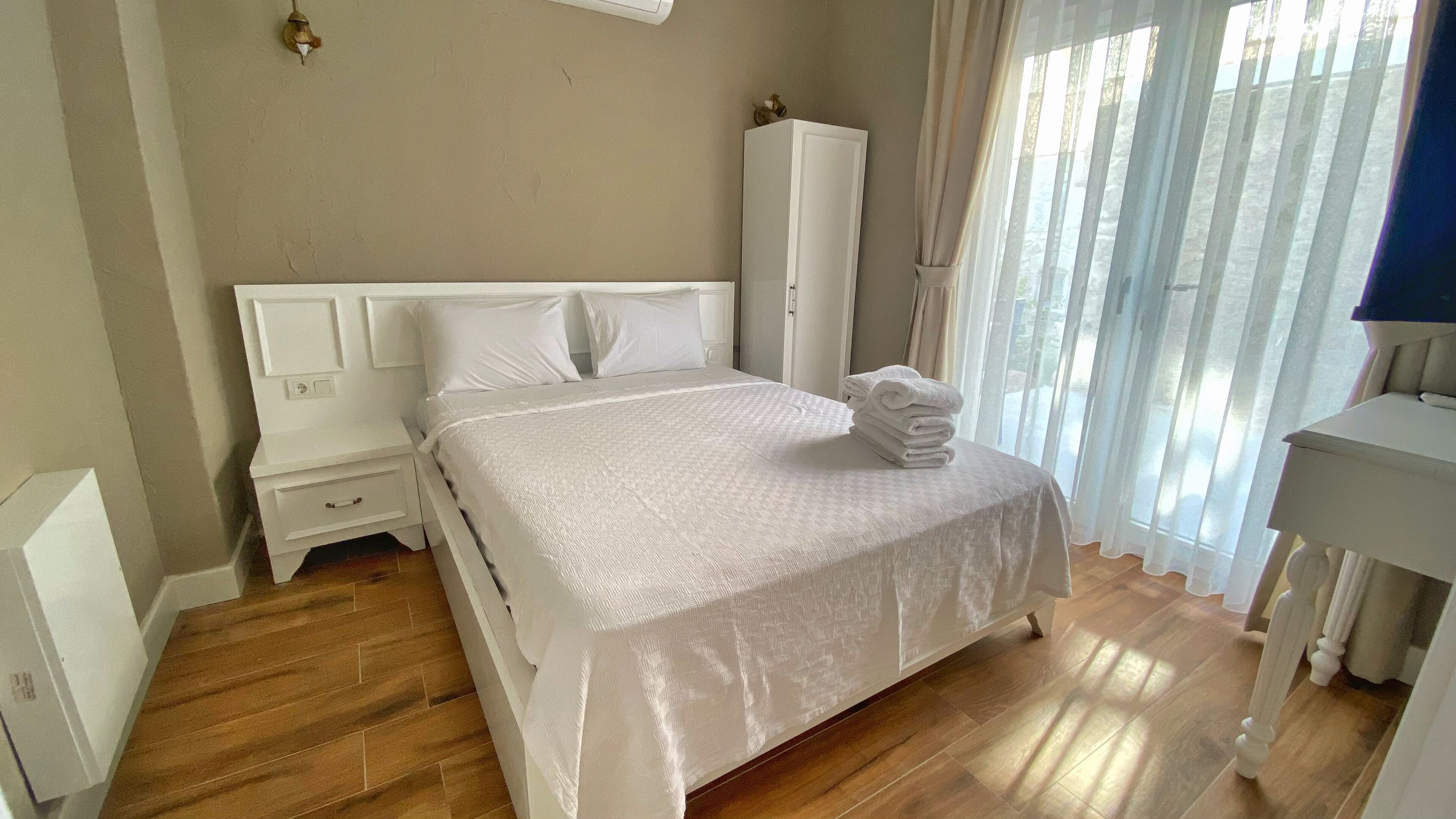 A neatly arranged bedroom with a bed, a nightstand, a wardrobe, and a bathroom area.