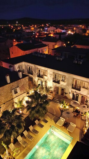 A hotel with a swimming pool, outdoor seating, and a view of the surrounding town at night. - Jardin d'Azur Alacati (Cesme)