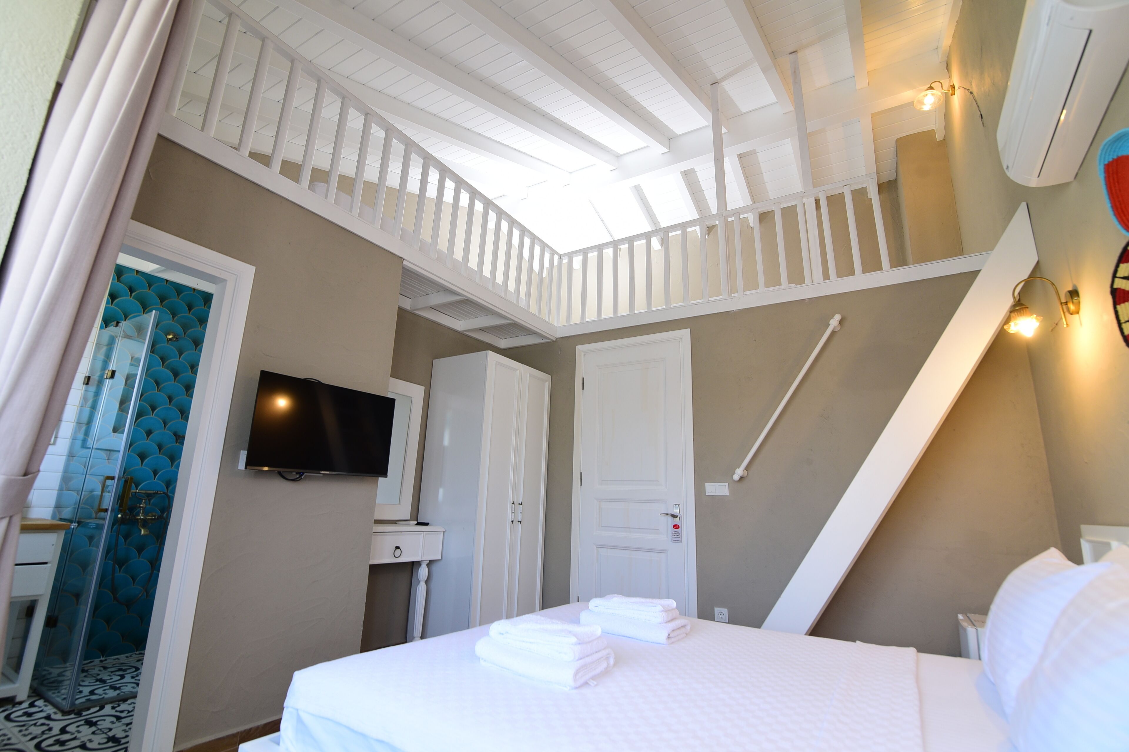 A hotel room with a bed, a TV, a bathroom, and a staircase.