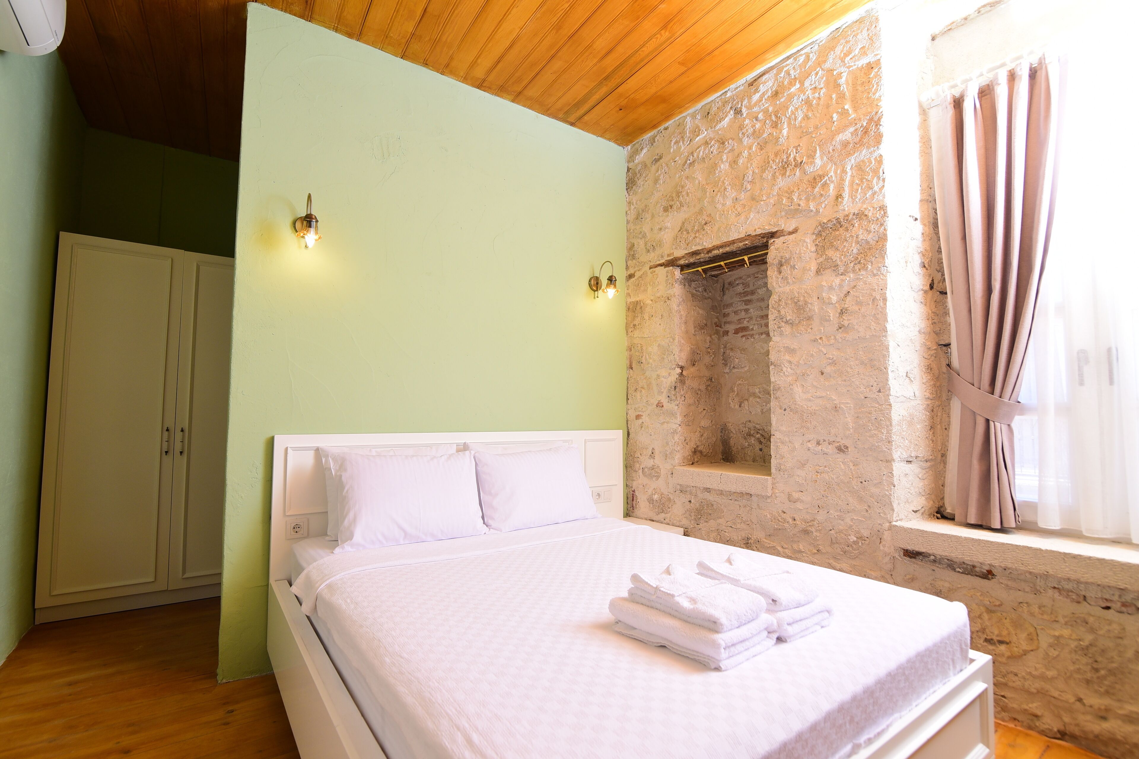 Un dormitorio con cama, armario, pared de piedra y ventana con cortinas.