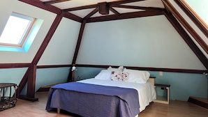 Camera da letto con soffitto a falde, un letto con biancheria bianca, un comodino e una finestra.
