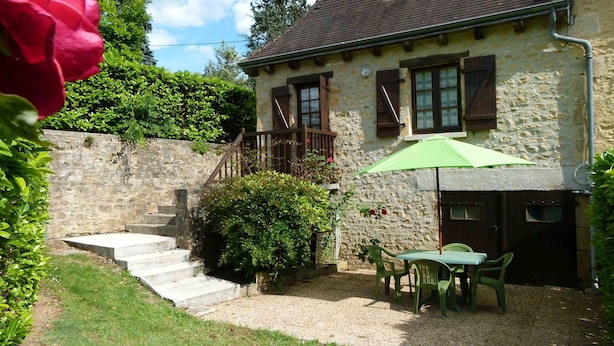 Una casa in pietra con una scala che conduce a un pontile in legno, un ombrellone verde e un tavolo con sedie.