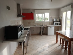 A kitchen with a gas stove, oven, red cabinets, a window, and a microwave.