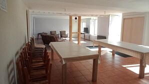 Une pièce spacieuse avec une longue table en bois et des chaises, un sol carrelé et une porte donnant sur une autre pièce.