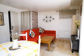 Un salon avec un canapé rouge, une table basse en bois, une table blanche recouverte d’une nappe jaune et un radiateur.
