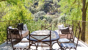 Eine Terrasse mit rundem Tisch und Stühlen, umgeben von einem Metallgeländer, mit Blick auf einen üppigen grünen Wald.
