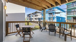 A covered outdoor area with a wooden table and chairs, overlooking a residential building complex. - Coastal Beach Condo (Carolina Beach)