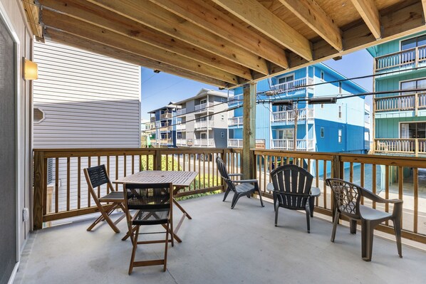 A covered outdoor area with a wooden table and chairs, overlooking a residential building complex. - Coastal Beach Condo (Carolina Beach)