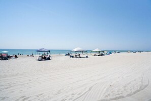 A beach with white sand, clear blue sky, and several beach umbrellas and tents. - Coastal Beach Condo (Carolina Beach)