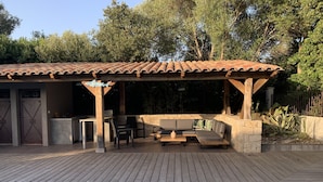 A poolside area with a covered seating area, a stone wall, and a wooden deck.