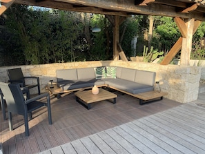 Et udendørs opholdsområde med træterrasse, stenvæg og træpergola.