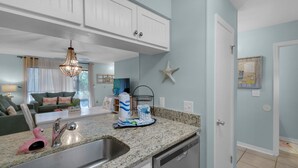 Eine moderne Küche mit Granit Arbeitsplatten, einer Edelstahlspüle und einem Geschirrspüler. Es gibt einen Essbereich mit Tisch und Stühlen sowie ein Wohnzimmer mit Sofa und einer Chandelier.