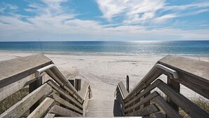 Eine Holztreppe führt zu einem Sandstrand mit freiem Blick auf den Ozean.