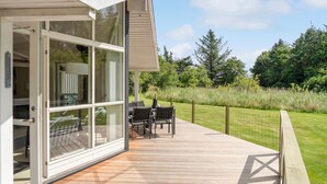 Ein modernes Haus mit einer großen Glasdoor, die auf eine Terrasse mit Gartenmöbeln führt.