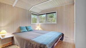 Ein Schlafzimmer mit einem Bett, zwei Kissen, einer Nachttischlampe und einem Fenster mit Blick auf Bäume.