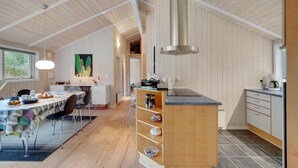 Eine moderne Küche mit Holzvertäfelung, einem Essbereich mit Tisch und Stühlen und einem großen Fenster, das viel Tageslicht hereinlässt.