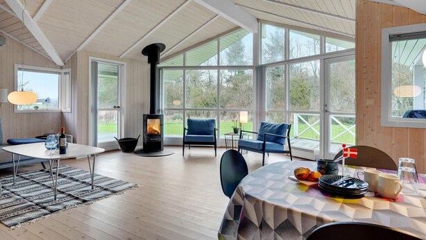 Ein gemütliches Zimmer mit großem Fenster, Kamin, Esstisch und bequemen Sitzgelegenheiten.