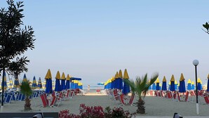 Un ristorante sulla spiaggia con posti a sedere all'aperto, ombrelloni blu e gialli e vista sulla spiaggia.